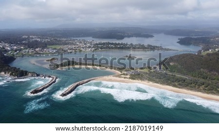 An aerial shot of Wagonga Head with hills and forest in the background under a cloudy sky