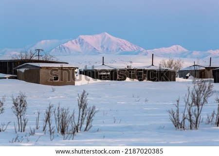 Winter arctic landscape. View of an abandoned settlement in the snowy tundra. Old houses among the snow. Hard-to-reach terrain in the Far North of Russia. Chukotka, Siberia. Polar region. Cold weather Royalty-Free Stock Photo #2187020385