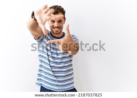 Handsome young man standing over isolated background smiling making frame with hands and fingers with happy face. creativity and photography concept. 