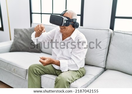Senior man playing video game using virtual reality goggles at home