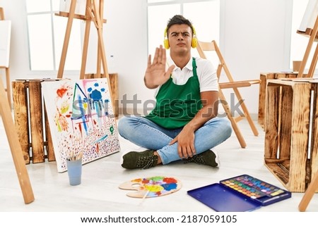 Young hispanic man at art studio doing stop sing with palm of the hand. warning expression with negative and serious gesture on the face. 