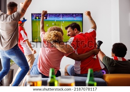 Group of young friends having fun watching football match on TV, drinking beer and cheering; football fans watching game at home celebrating after their team scoring a goal Royalty-Free Stock Photo #2187078117