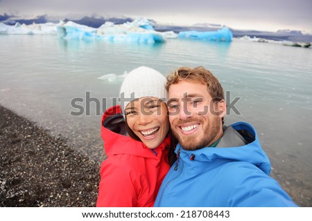 Couple taking selfie self portrait photo by Jokulsarlon glacial lagoon / glacier lake on Iceland. Happy tourists on travel enjoying beautiful Icelandic nature landscape with Vatnajokull in backround.