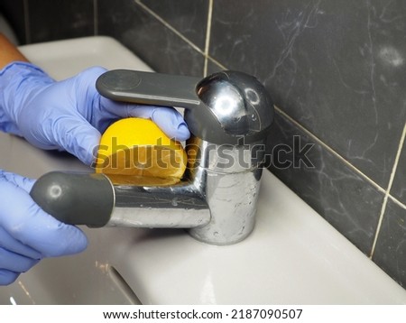 The chrome faucet of the sink in the bathroom is cleaned of limescale with a lemon. Close-up. The concept of ecological cleaning of the house without the use of household chemicals.