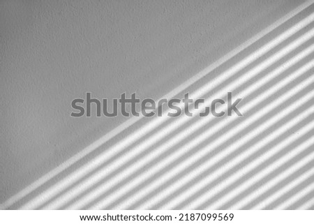 Abstract shadow lines from the curtain on the grey wall. Beautiful window blind shadow from morning sunlight on grey empty wall inside the room. Royalty-Free Stock Photo #2187099569