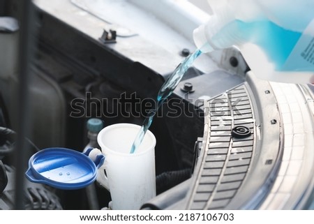 Flow windshield fluid into the windshield washer reservoir. Water tank wiper on car engine room, Maintenance concept. Royalty-Free Stock Photo #2187106703