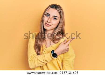 Beautiful hispanic woman wearing casual yellow sweater pointing with hand finger to the side showing advertisement, serious and calm face 