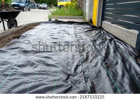 The plowed garden in front of the fence in the house, covered with black agrofiber, visible black plastic pin. Royalty-Free Stock Photo #2187133225