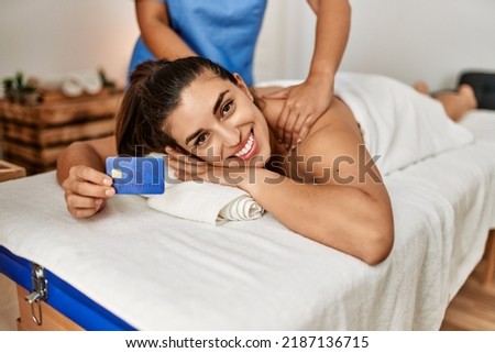 Two women therapist and patient having massage session holding credit card at beauty center