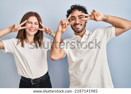 Young couple wearing casual clothes standing together doing peace symbol with fingers over face, smiling cheerful showing victory 