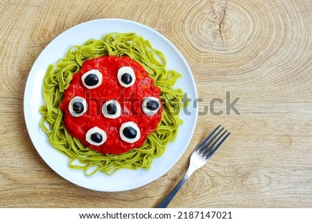 Halloween monster pasta-spinach fettuccine pasta with tomato sauce,mozzarella cheeses and black olives on plate with wooden background.Creative food idea for halloween's dinner.Top view.Copy space