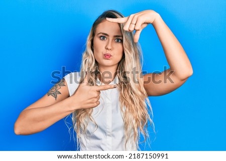Beautiful young blonde woman doing picture frame gesture with hands puffing cheeks with funny face. mouth inflated with air, catching air. 