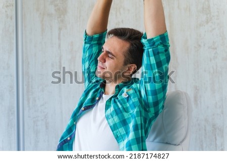 A man is stretching and holding his neck because of neck and back pain from long sitting on his chair while working in his home office during the day
