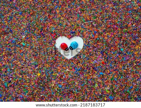 Textured background of colored crayon shavings with a white heart in the center and, in the middle of it, two ladybugs face to face with love