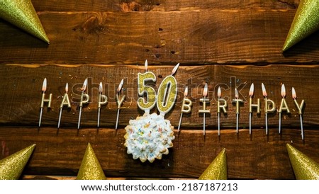 golden letters of the candle with the number happy birthday, the background of the pie with candles happy birthday on the background of brown stranded boards. Postcard Happy birthday 50