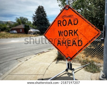 Orange road work ahead sign near road and sidewalk