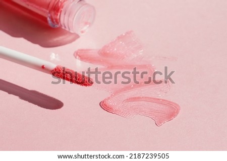 Smears of shining lip gloss and lip gloss brush on pink background, hard shadows Royalty-Free Stock Photo #2187239505