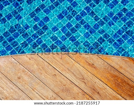 Top view of empty wooden plank table or deck floor curved shape in front of the blurred background of blue mosaic tiles grid pattern in swimming pool. Empty space on poolside, summer background.
