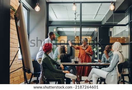 Successful businesswomen high fiving each other during an office meeting. Two cheerful businesswomen celebrating their achievement. Happy businesspeople working as a team in a multicultural workplace. Royalty-Free Stock Photo #2187264601