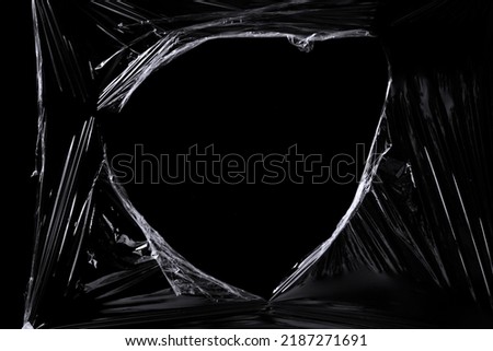 a black transparent plastic texture with hole for poster and cover art. realistic plastic wrap for overlay, copy space and photo effect. wrinkled plastic surface on black background Royalty-Free Stock Photo #2187271691