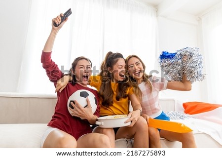 Group of Asian woman friends sitting on sofa and watching soccer games world cup competition on television together at home. Sport fans people shouting and celebrating sport team victory match.