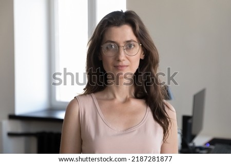 Head shot portrait of attractive businesswoman posing at workplace. Company office employee, serious businesslady in glasses staring at camera. Workforce, hr, professional occupation person concept