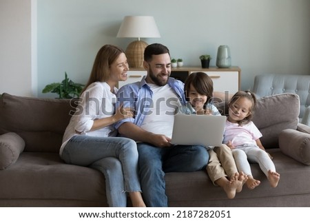Young couple and siblings sit on couch spend leisure on internet using computer, watch favourite on-line videovlog, resting at home. Children development, modern tech, e-shopping, make order concept
