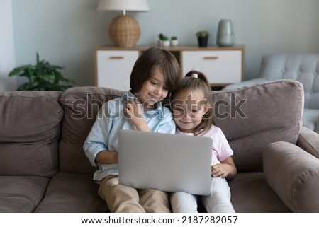 Preschooler children sit on sofa with laptop spend time on internet, enjoy favourite video vlog, watch cartoons use modern wireless tech. Device overuse of young gen, parental control software