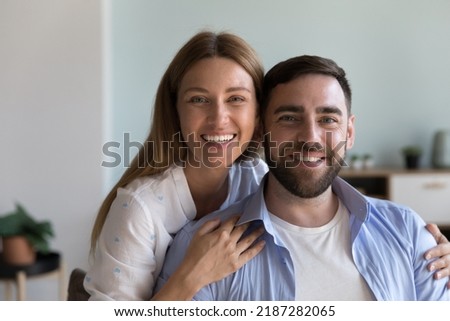 Enamoured couple posing for camera. Beautiful woman hugs her beloved husband smiling looking at cam feeling love. Head shot portrait of well-being spouses, medical insurance cover for family concept Royalty-Free Stock Photo #2187282065