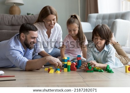 Young parents and little children play wooden multicolored bricks, sit on warm floor in living room spend weekend pastime at modern flat, enjoy game and communication. Kids development, fun concept Royalty-Free Stock Photo #2187282071