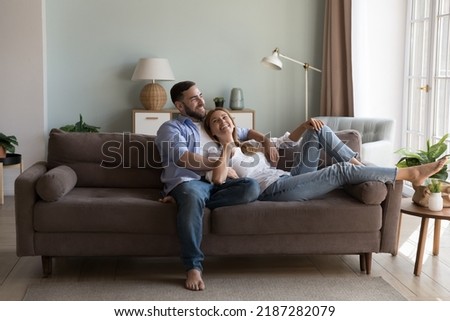 Relaxed couple in love enjoy conversation resting on sofa in fashionable living room, share dreams, planning future and children, spend time at modern home. Daydreams, romantic relations, date Royalty-Free Stock Photo #2187282079