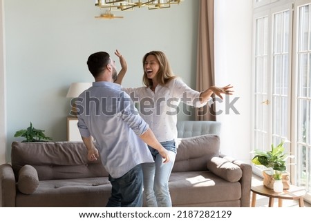 Hilarious millennial beautiful couple dance together in cozy sunny living room. Happy homeowner family celebrate first day at own flat. Bank loan, independence, romantic date and relationships Royalty-Free Stock Photo #2187282129