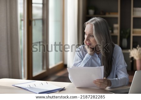 Thoughtful elderly retired woman thinking over paper documents, analyzing agreement terms, checking bills at home table, getting troubles, making decision, feeling doubt, Royalty-Free Stock Photo #2187282285