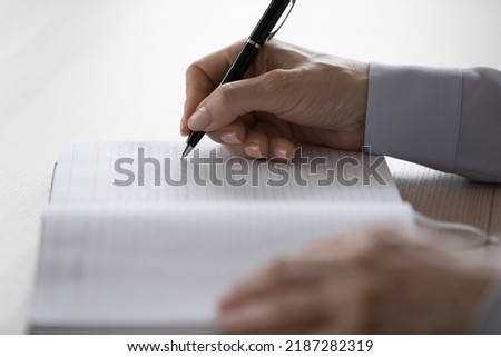 Hands of adult woman writing notes in notebook. Side view, close up of page with handwritten text and pen. Mature female writer, professional author working on book