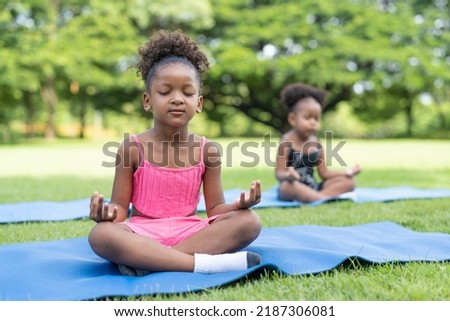 African American little girls sitting with closed eyes practicing meditate yoga on roll mat in the park. Kids afro girls with curly hair engaged training yoga in outdoor. Royalty-Free Stock Photo #2187306081