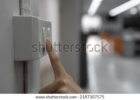The young woman's hand turned off the light switch in the office. Energy saving concept. selective focus Royalty-Free Stock Photo #2187307575