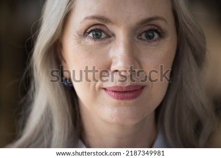 Happy pretty senior woman close up facial portrait. Attractive grey haired retired lady, pensioner, older mature female model with natural makeup looking at camera, posing. Cropped shot
