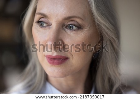 Pensive dreamy middle aged senior woman face close up. Pretty retired woman, pensioner, beauty care model with makeup looking away. Elderly age concept. Cropped shot
