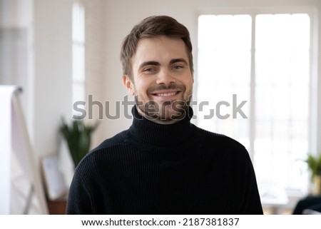 Head shot of happy male millennial posing in white interior. Profile picture of confident young man in black casual sweater looking at camera and smiling. Job candidate or employee corporate