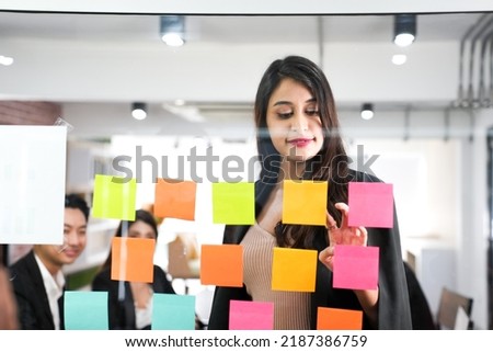 Thinking businesswoman writing on colorful notes attached to a glass wall the entrepreneur creates planning visual list.