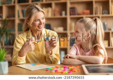 Happy woman speech therapist teaching little girl with pronounciation deffects to say sound R during personal training at classroom Royalty-Free Stock Photo #2187390655