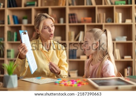 Cheerful female speech therapist curing girl's problems and impediments, cute child learning and pronouncing letters with private English language tutor during lesson Royalty-Free Stock Photo #2187390663