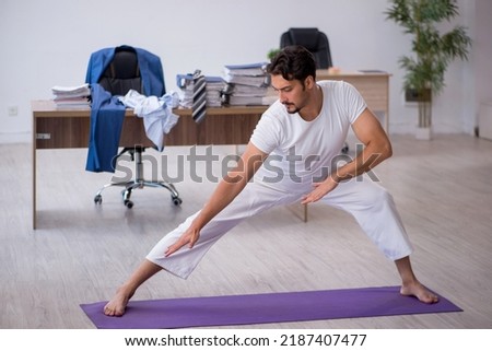 Young male employee doing sport exercises in the office