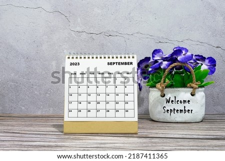 September 2023 desk calendar on wooden desk with potted plant.