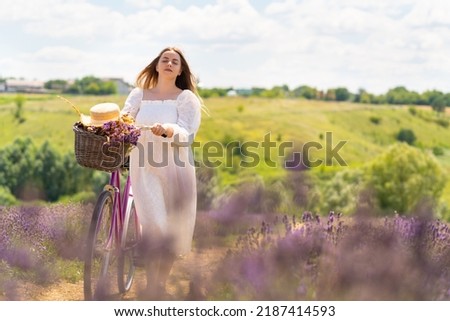 Serene young woman enjoying a day in the countryside wheeling her bicycle through a field of lavender with eyes closed and a contented smile