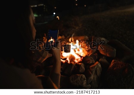 Woman takes a picture of a mug near the campfire. Close up.