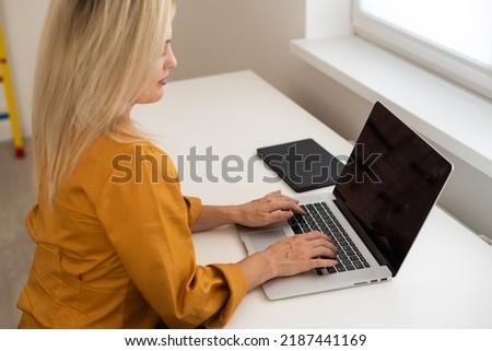 Image of young beautiful joyful woman smiling while working with laptop in office.