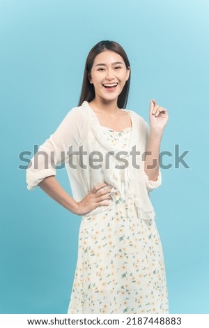 Beautiful young asian woman in white dress with flower pattern feeling surprise isolated on blue background