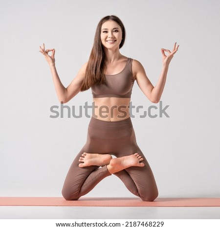 Fit asian woman in sportswear practicing yoga, keeping balance, while standing on a knees in difficult lotus pose. Healthy lifestyle, yoga, stretching, fitness concept. Square composition.