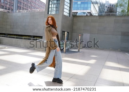 Cool teen stylish redhead fashion hipster girl model walking in big city subway. Beautiful teenage girl with red hair wearing trench coat going in urban location. Royalty-Free Stock Photo #2187470231